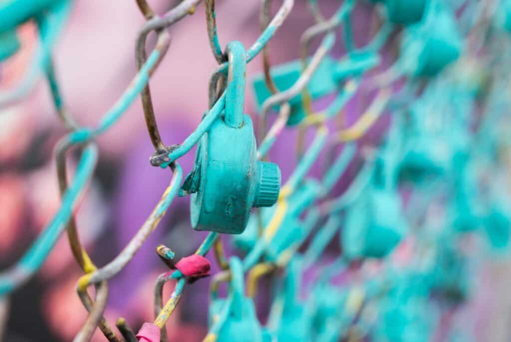 image of a pad-lock painted in teal hanging from a colourful wire fence for the article GDPR Guidance: ICO Announces What It Will Publish And When