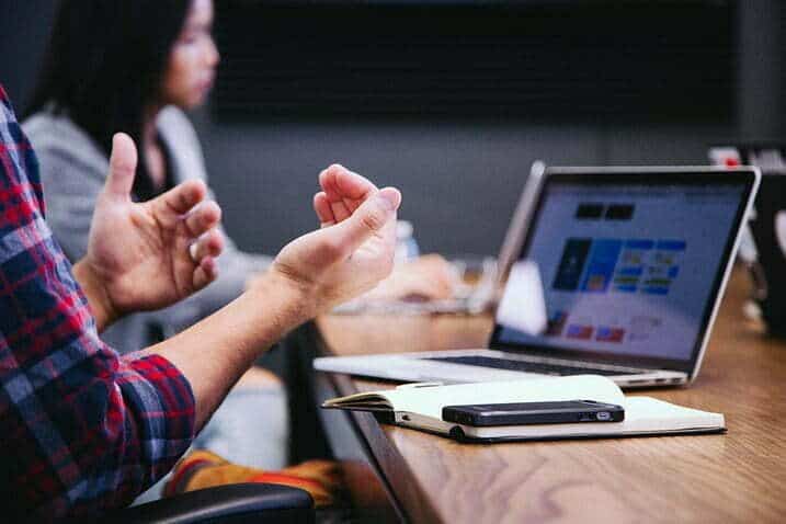 image of a meeting showing one person's hands making gestures in focus and the laptop and other person blurred for the article people buy from poeple