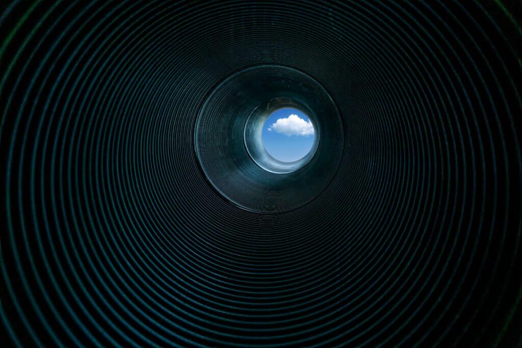 low angle of pipe interior to show cloud in blue sky at end of tube representing successful sales pipelines