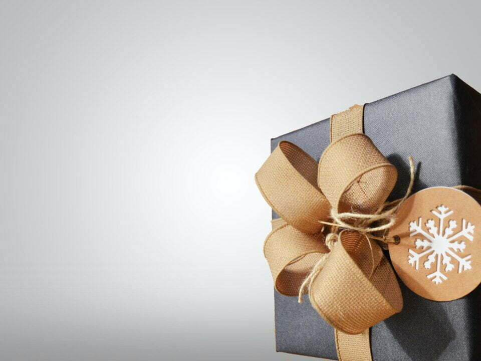 picture of present with blue wrapping paper, gold ribbon tied up in a bow and a label with a snowflake on it in front of a greay background, for christmas marketing planning article