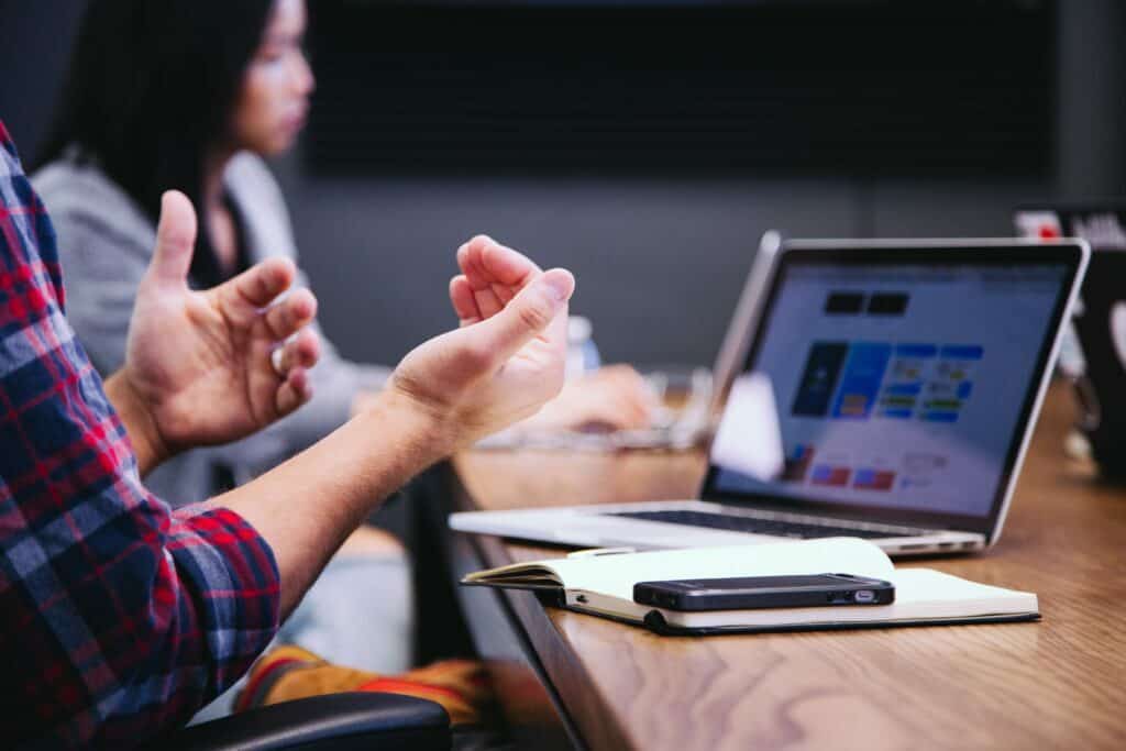 black smartphone on notebook and laptop near person gesturing in conversation in meeting for how to plan your 90 marketing plan article