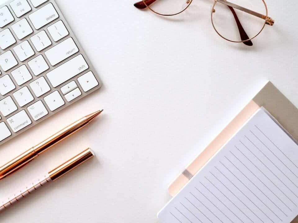 laptop pens glasses and notepad on white surface for how to make a 90 day marketing plan article