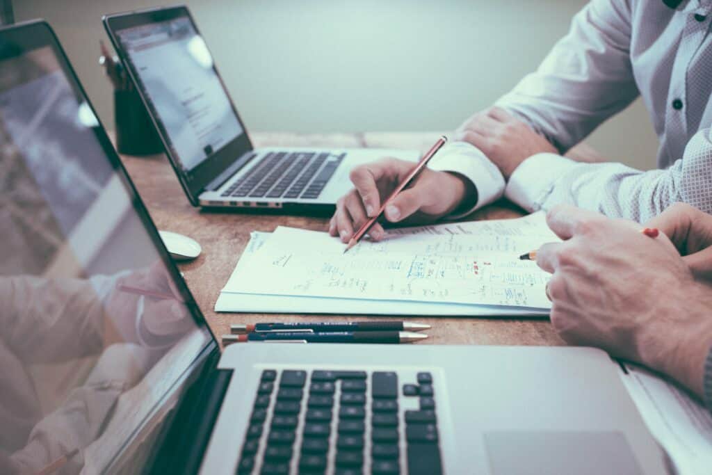 person holding pencil near laptop planning for how to plan your 90 marketing plan article