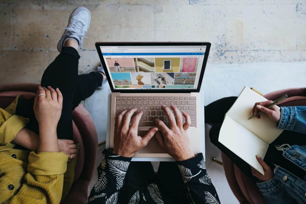 top-down shot of three looking at images on laptop with a notebook in one person's lap, planning a campaign, for guerrilla marketing article