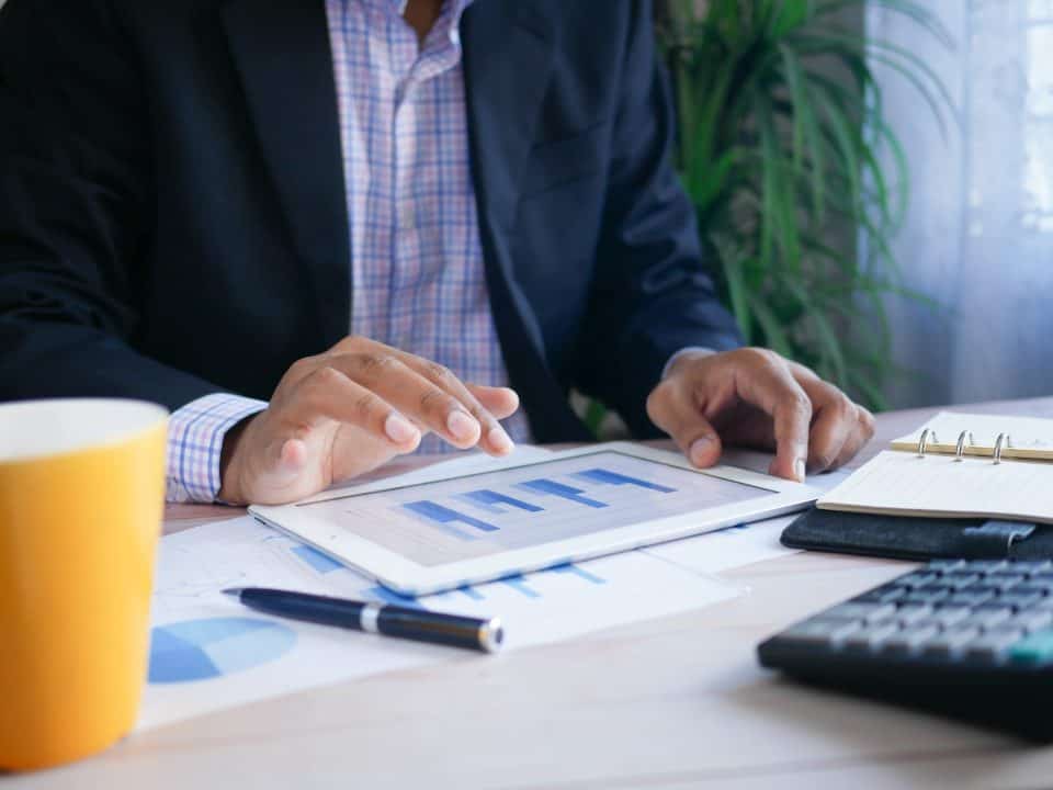 person looking at graph on ipad next to yellow coffee cup and calculator in a business setting for crm comparison article