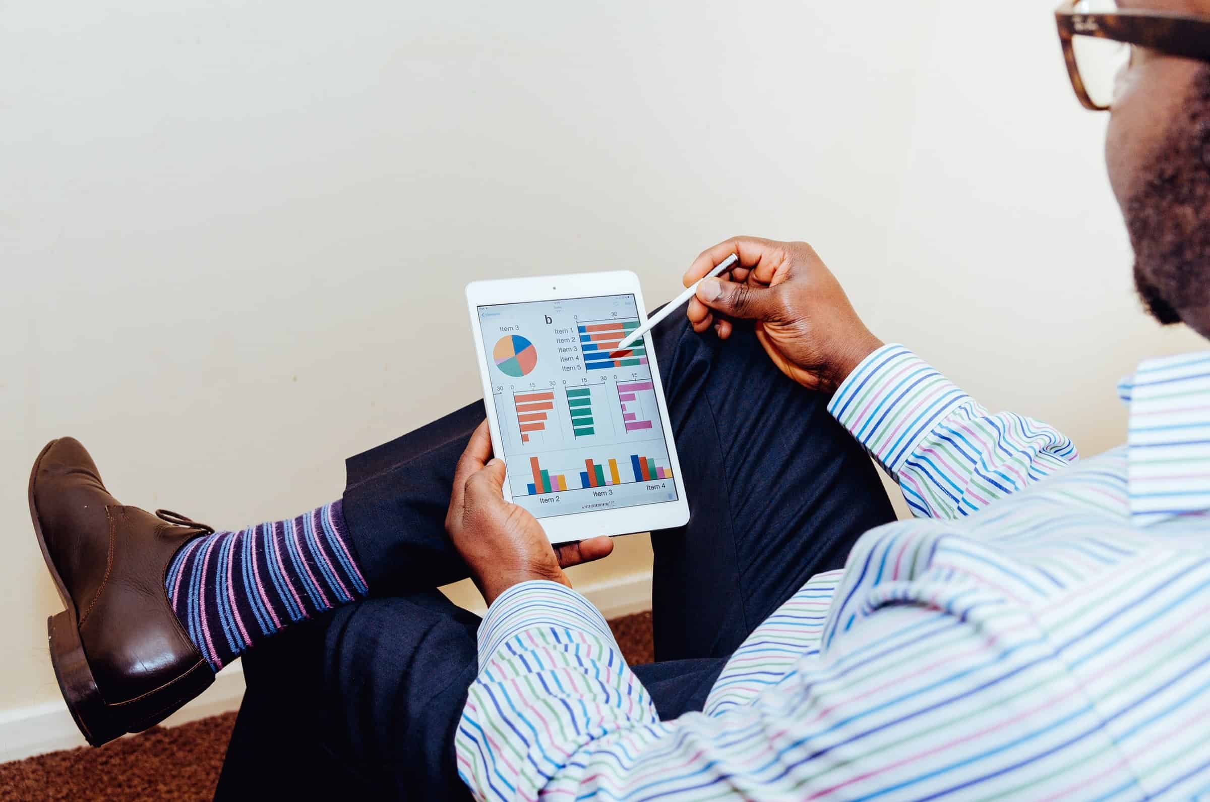 man in glasses sitting down looking at pie charts on tablet for strengthening customer communications article