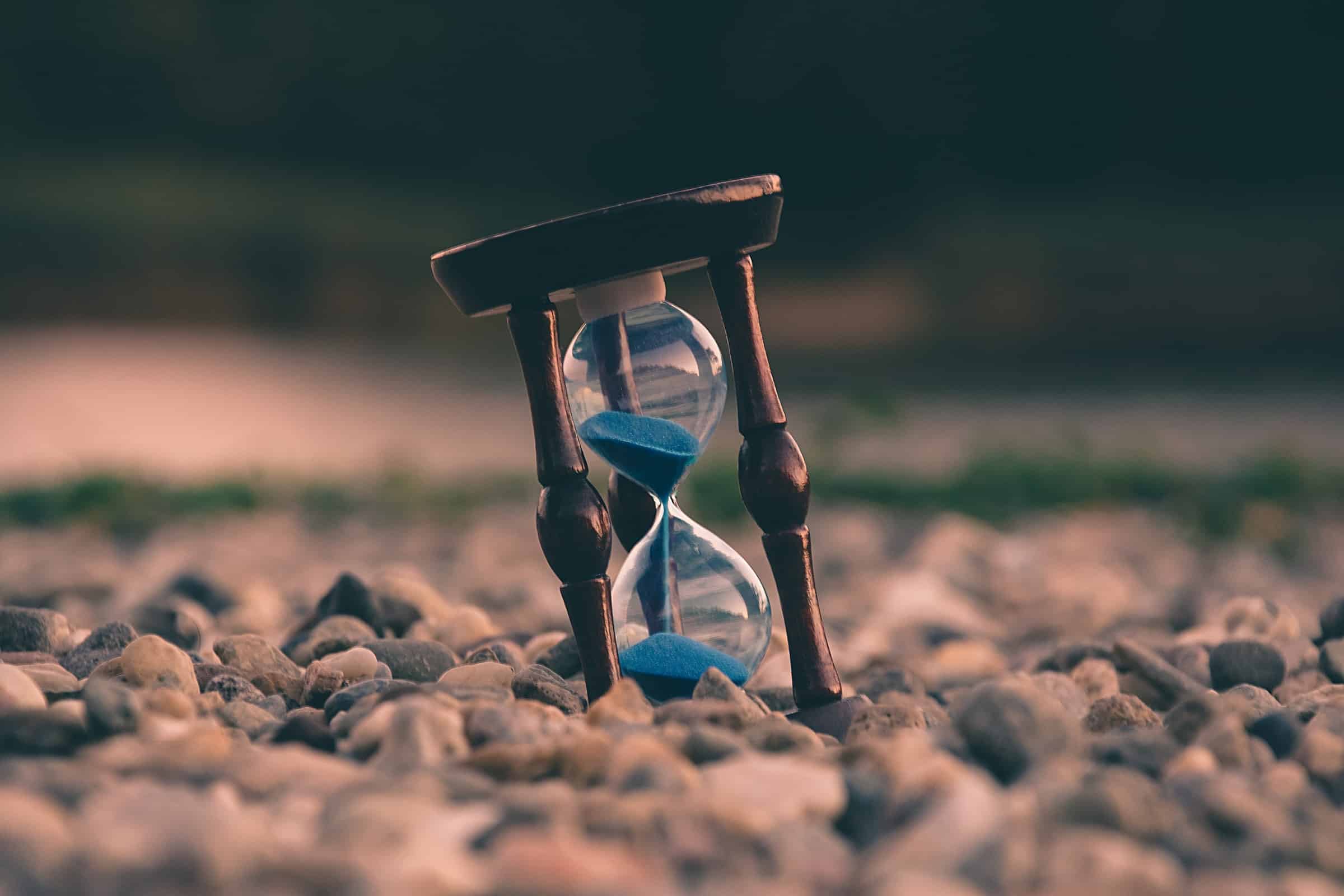 selective focus photo of wooden hourglass with blue sand on stones for sales planning article