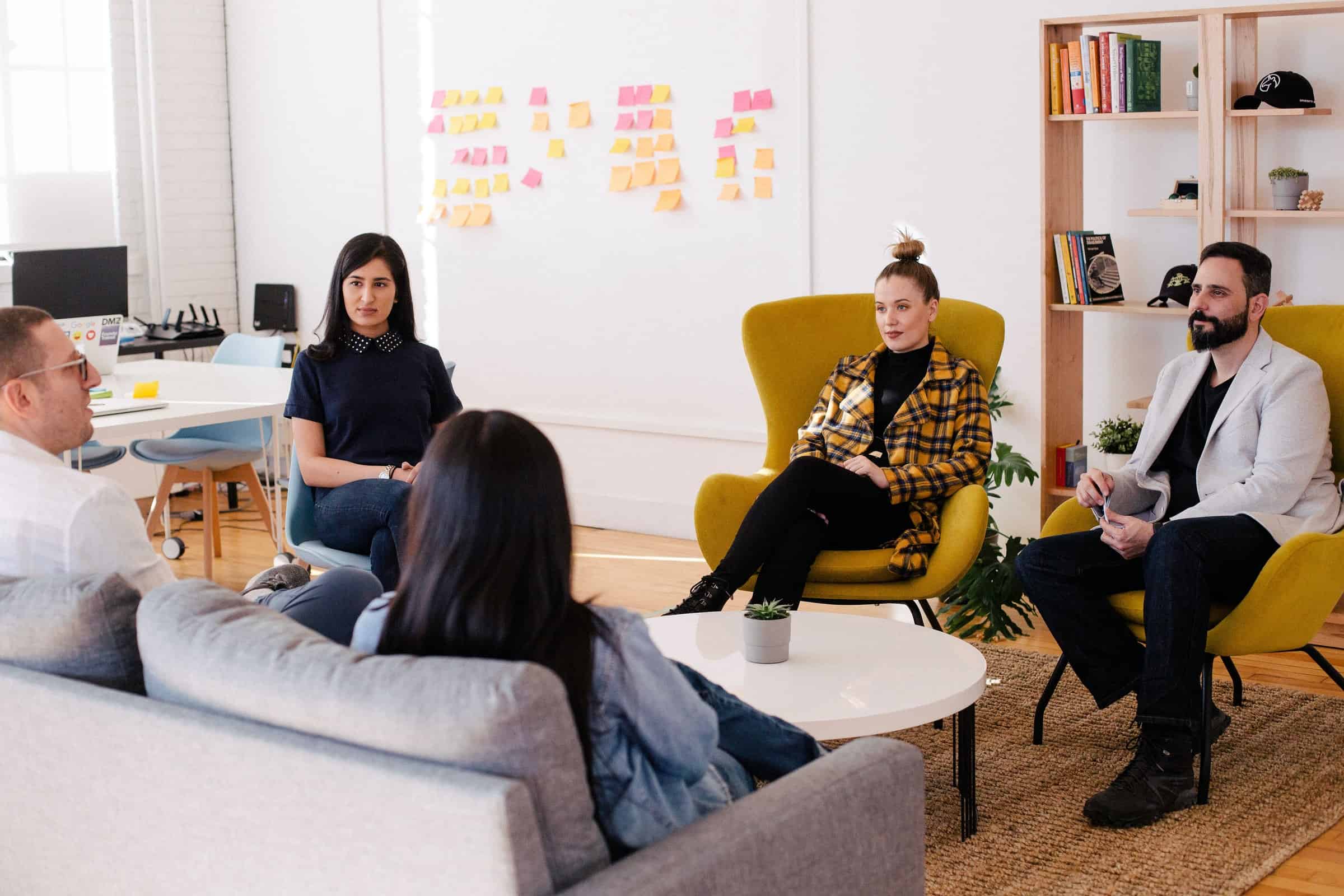 a group of professional in a bright office sat around a white coffee table on chairs and a sofa having a conversation for sales planning article