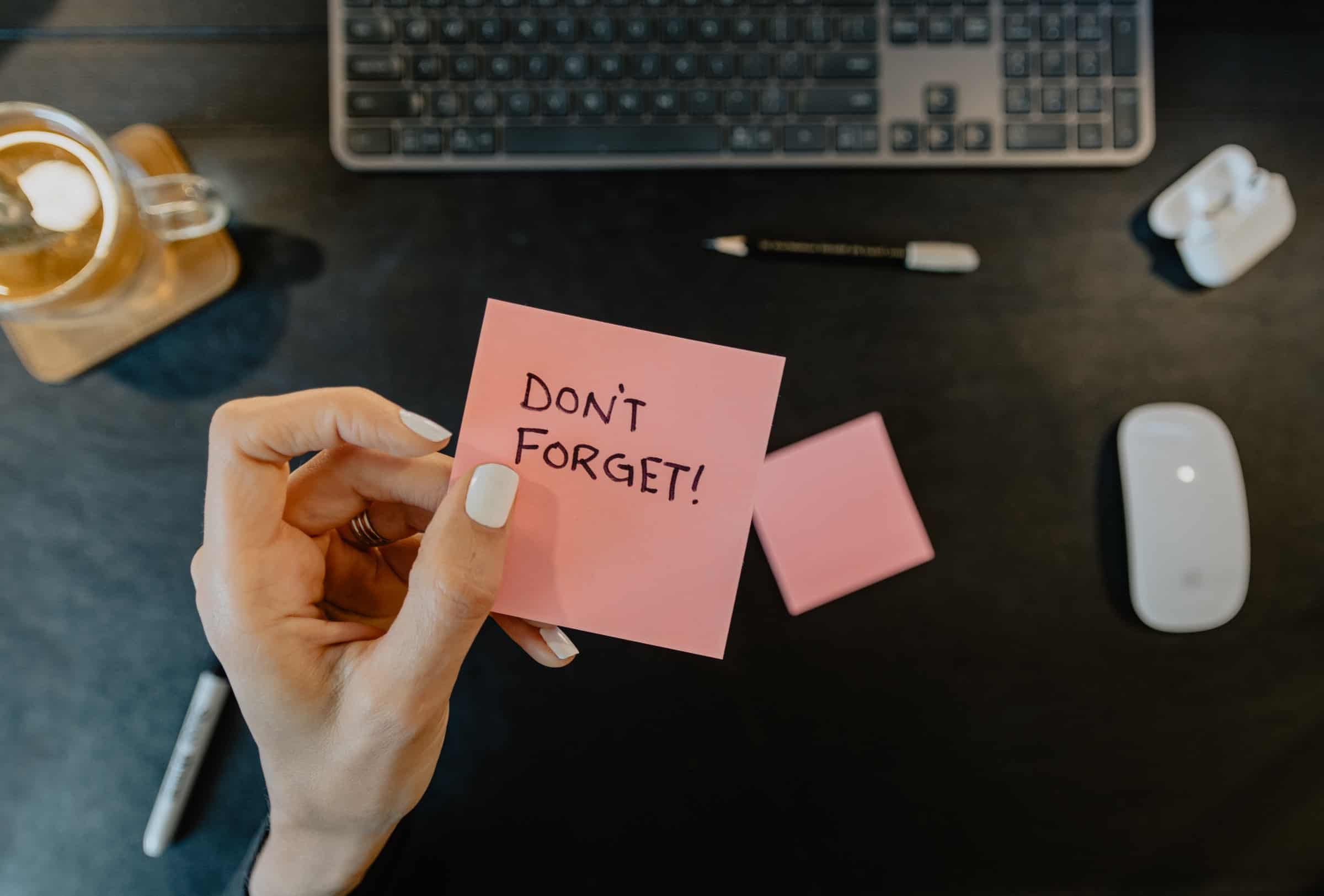 hand holding pink sticky note that says 'don't forget!' with laptop, mouse and coffee in background for never forgetting a followup article