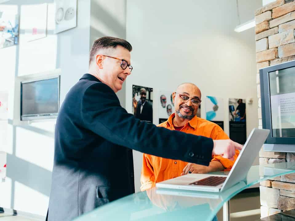 two men in a brightly lit office looking at a laptop for sales pipelines sales process management article