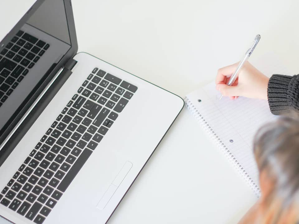 woman writing on notebook looking at laptop photo for making sales notes featured image