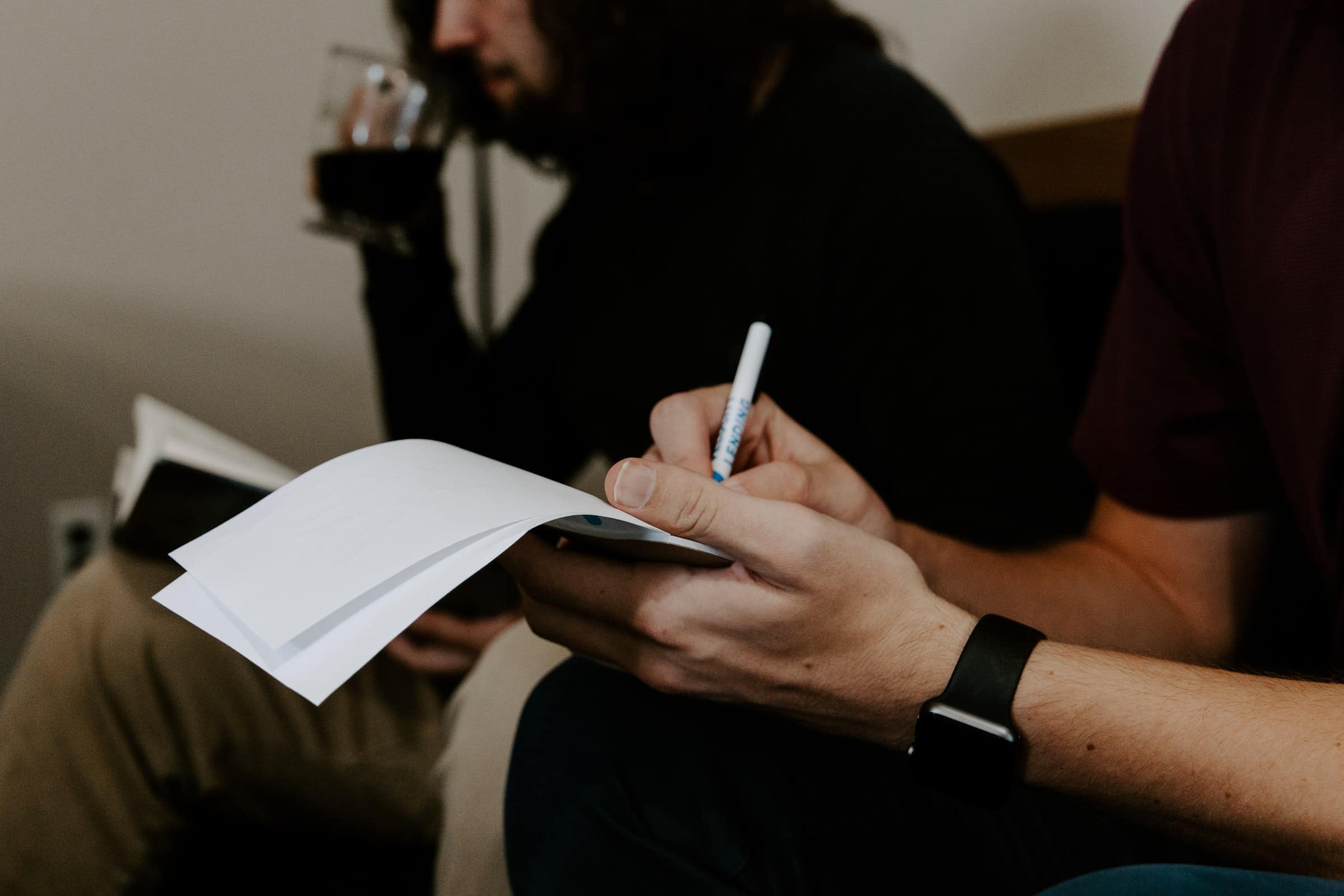 man writing on notepad beside man for sales notes article