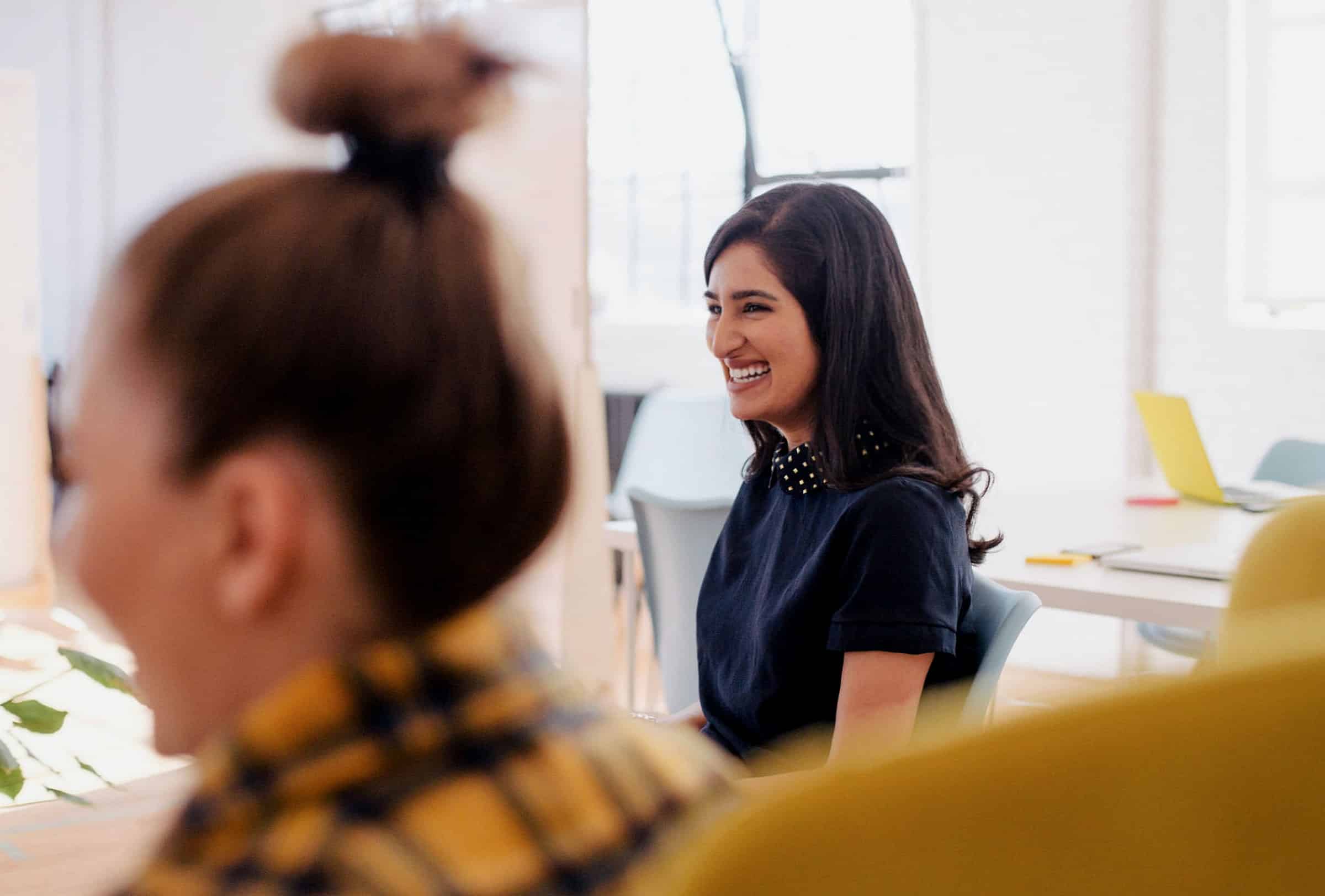 smiling woman in navy blue shirt sitting down at work meeting for growth for business article