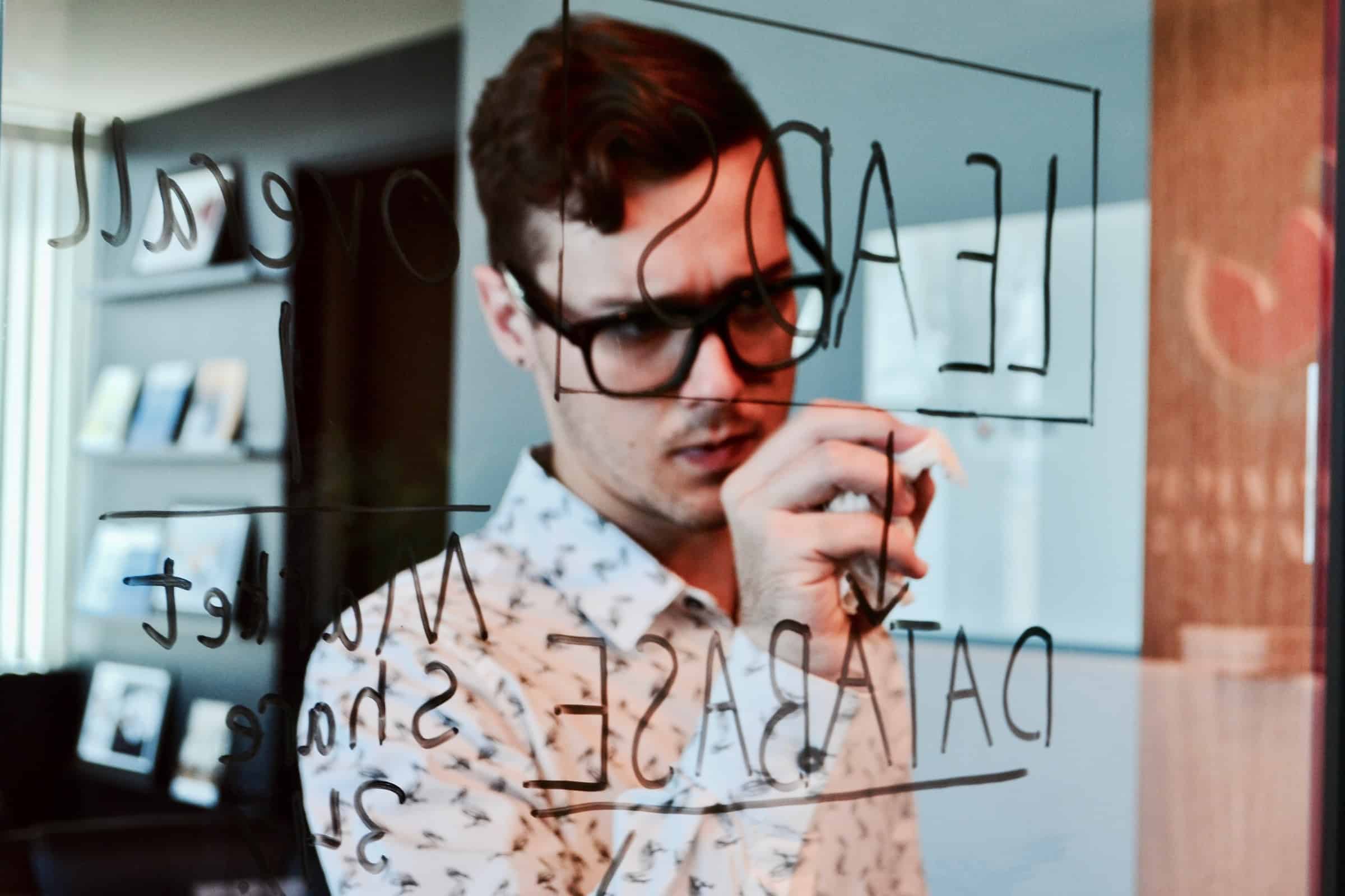 man with glasses planning lead generation strategy on transparent board for what crm features article