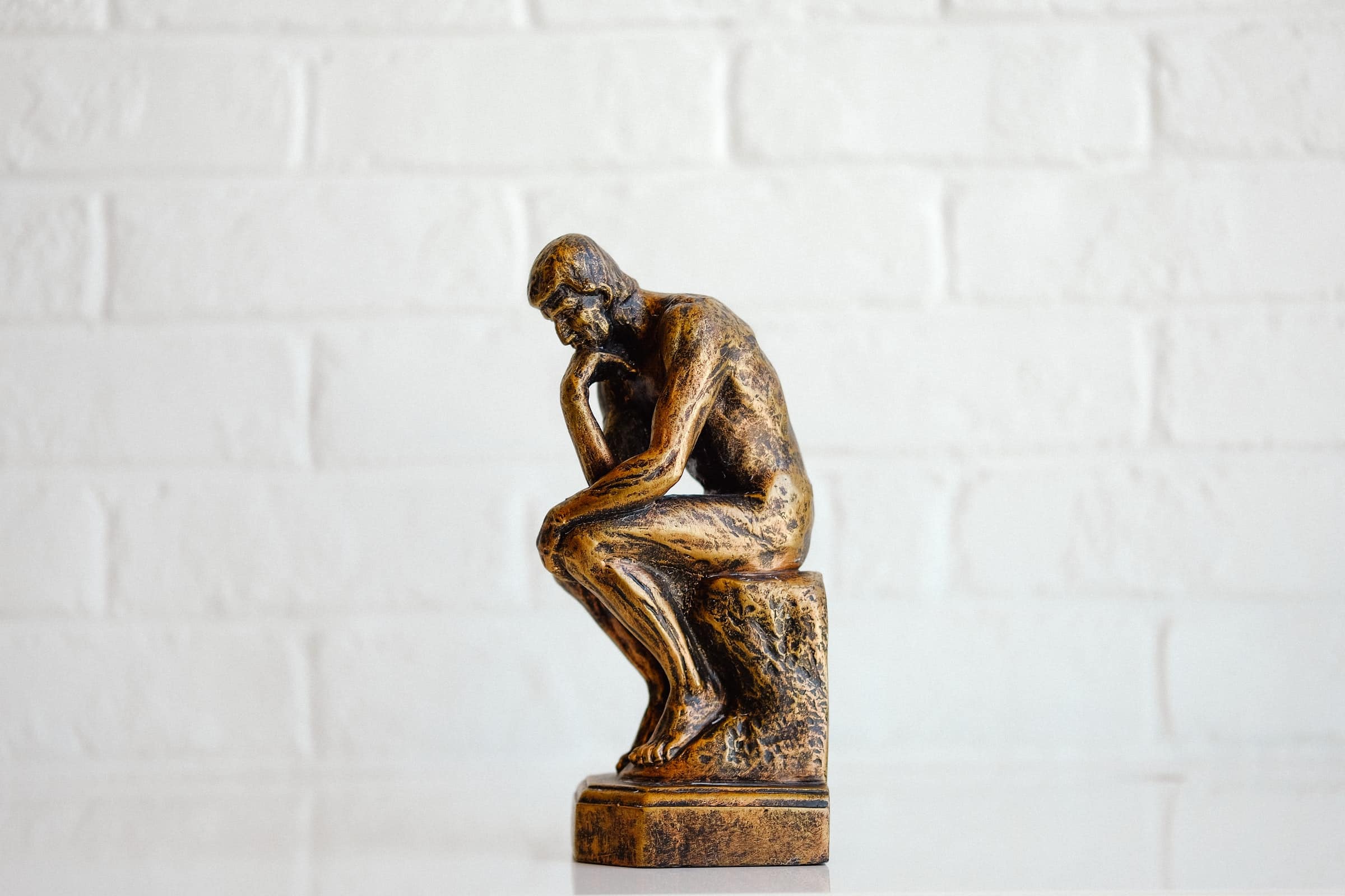 bronze miniature of the thinker in front of white brick wall for lost customer article